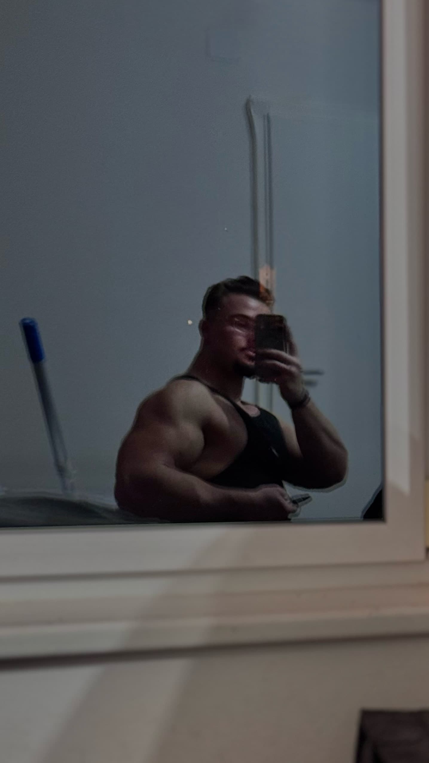 Muskulöser Mann im schwarzen Tanktop macht ein Spiegel-Selfie und zeigt seine trainierten Arme.