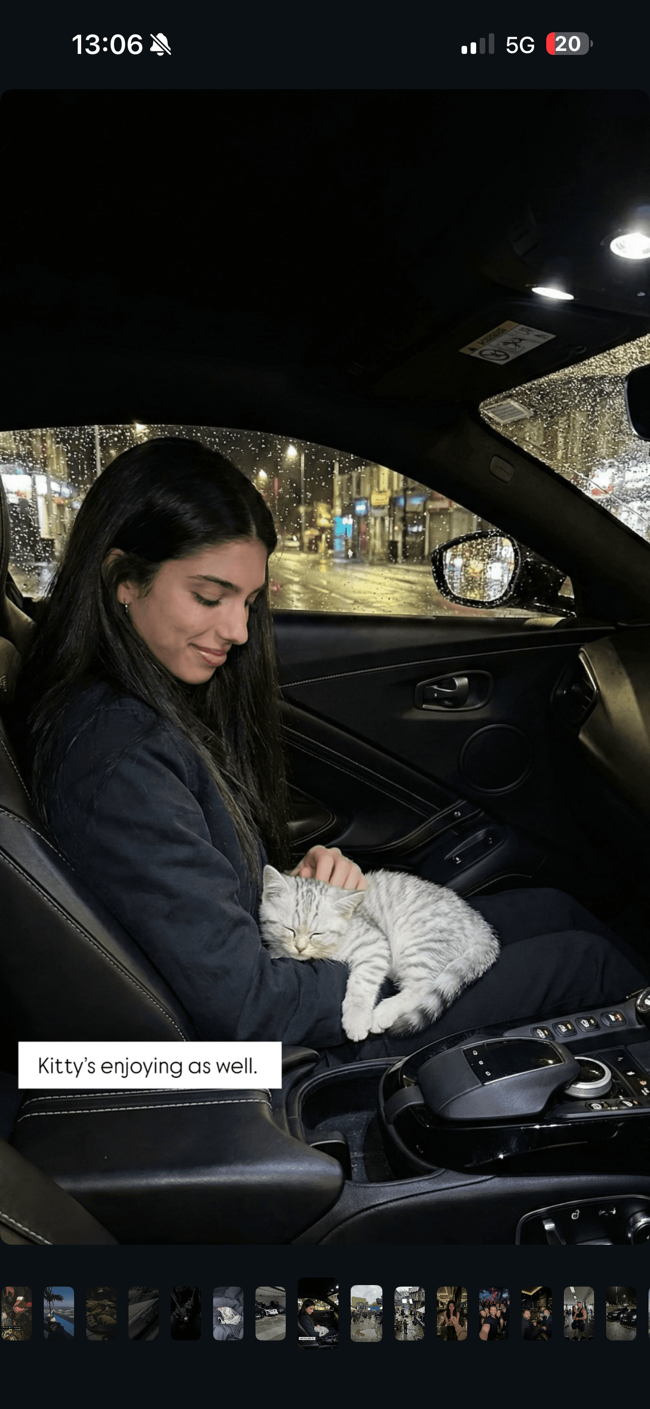 Eine lächelnde Frau streichelt ein schlafendes grau gestreiftes Kätzchen nachts in einem verregneten Auto.